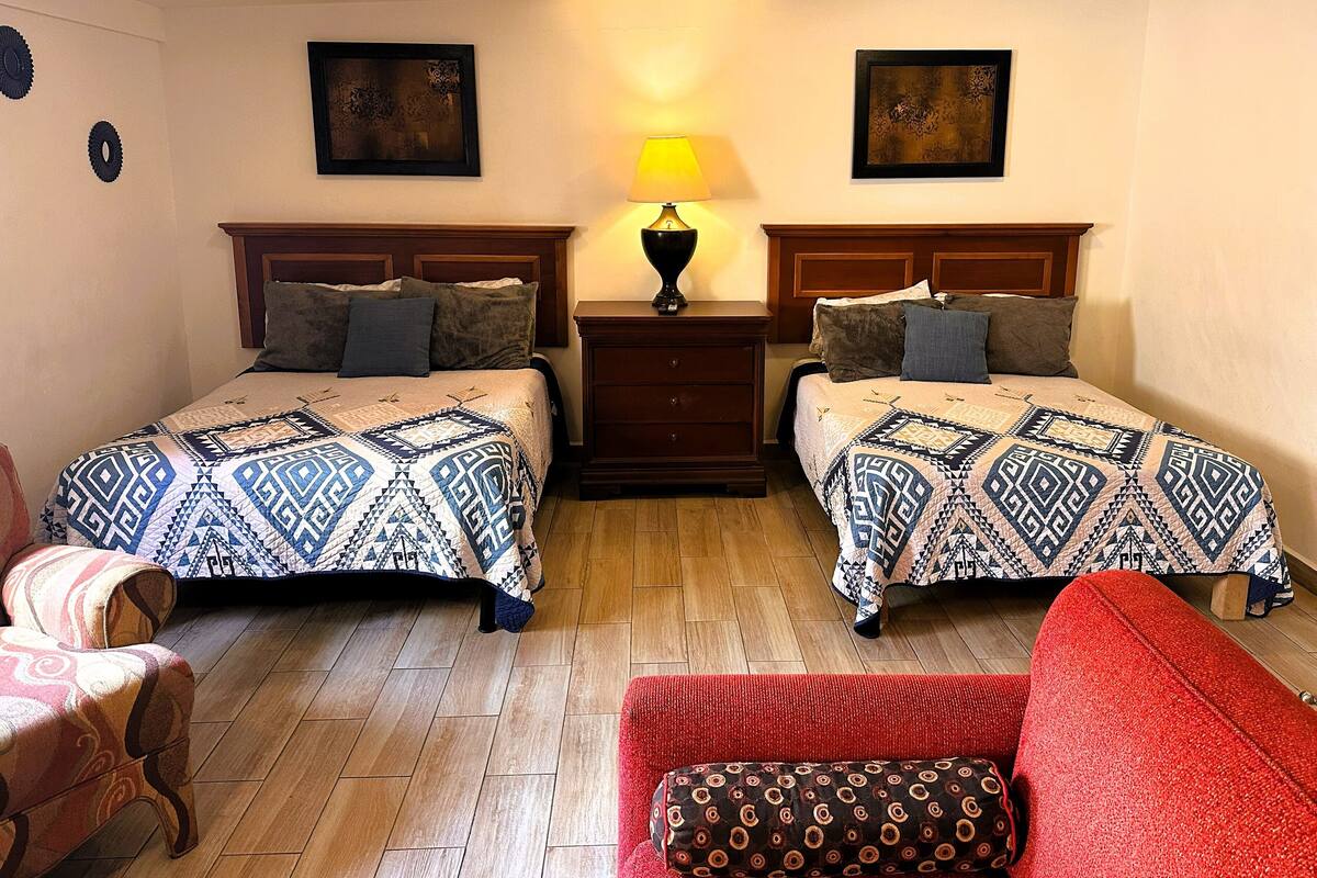 Habitación de hotel con dos camas, una mesita de noche, una lámpara y una silla roja.
