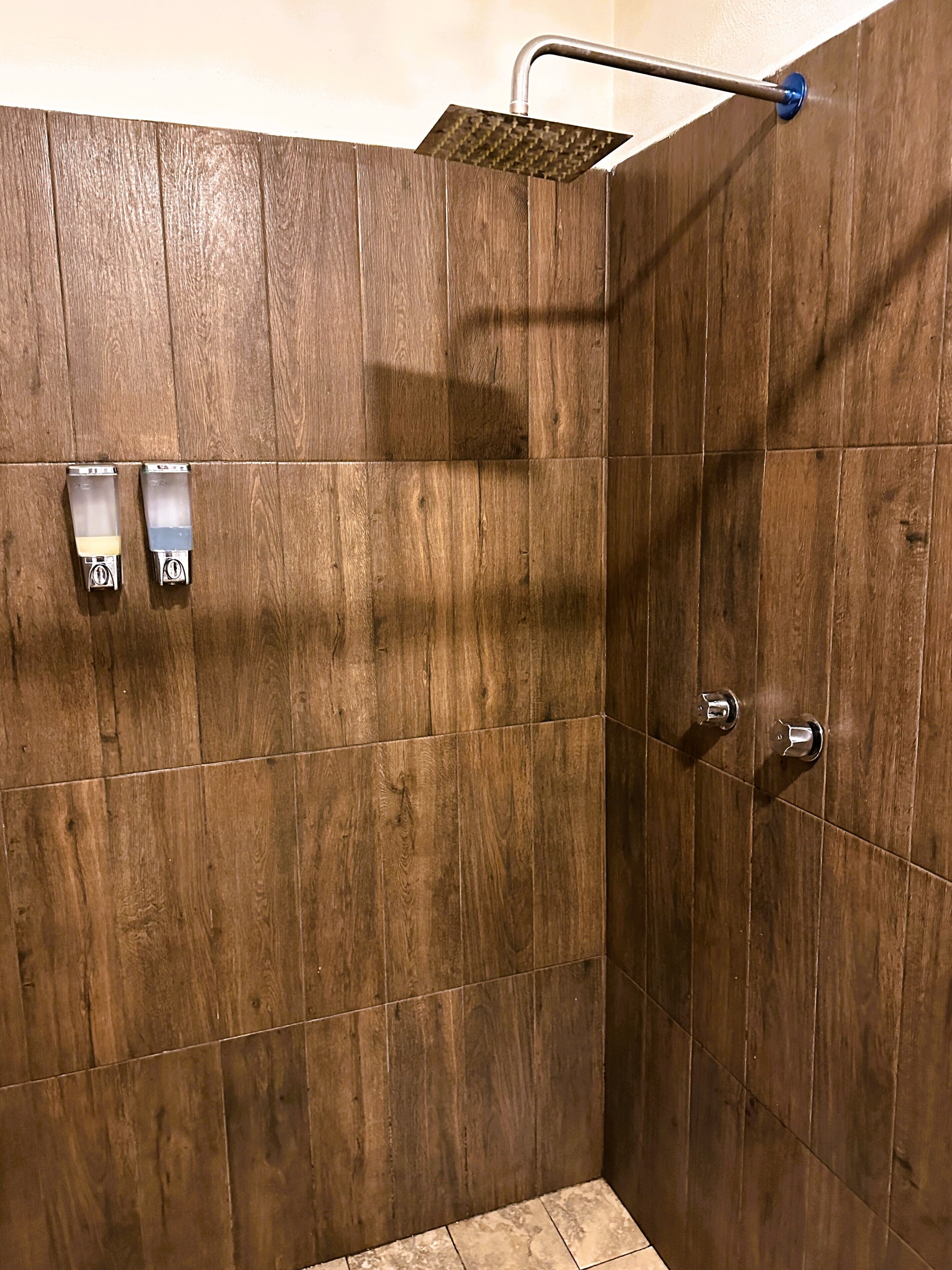 A shower area with a wooden wall, a showerhead, and two towel dispensers.