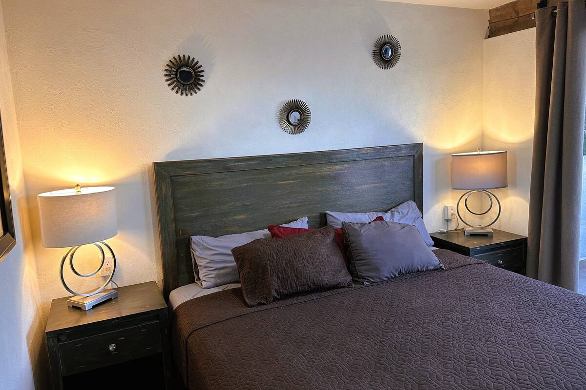 Una cama bien tendida con cabecera oscura, dos lámparas de noche y apliques decorativos en la pared.
