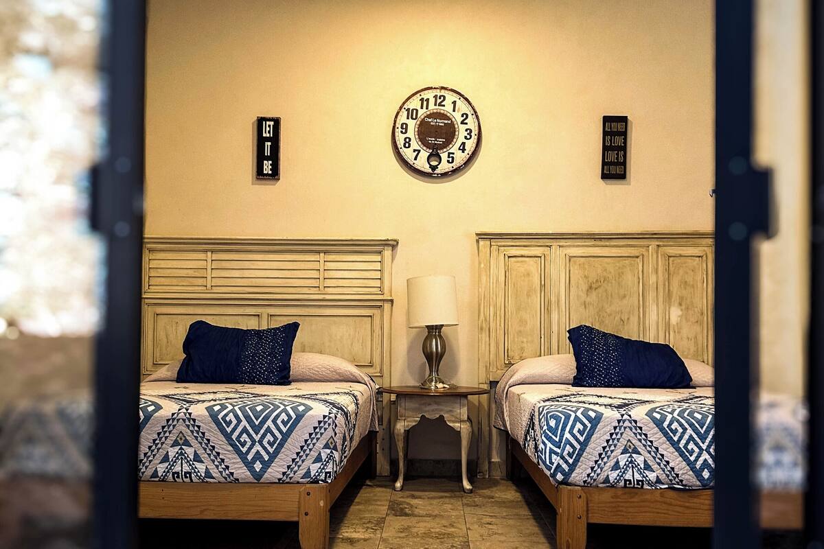 Una habitación con dos camas, un reloj de pared y una pequeña mesa con lámpara.
