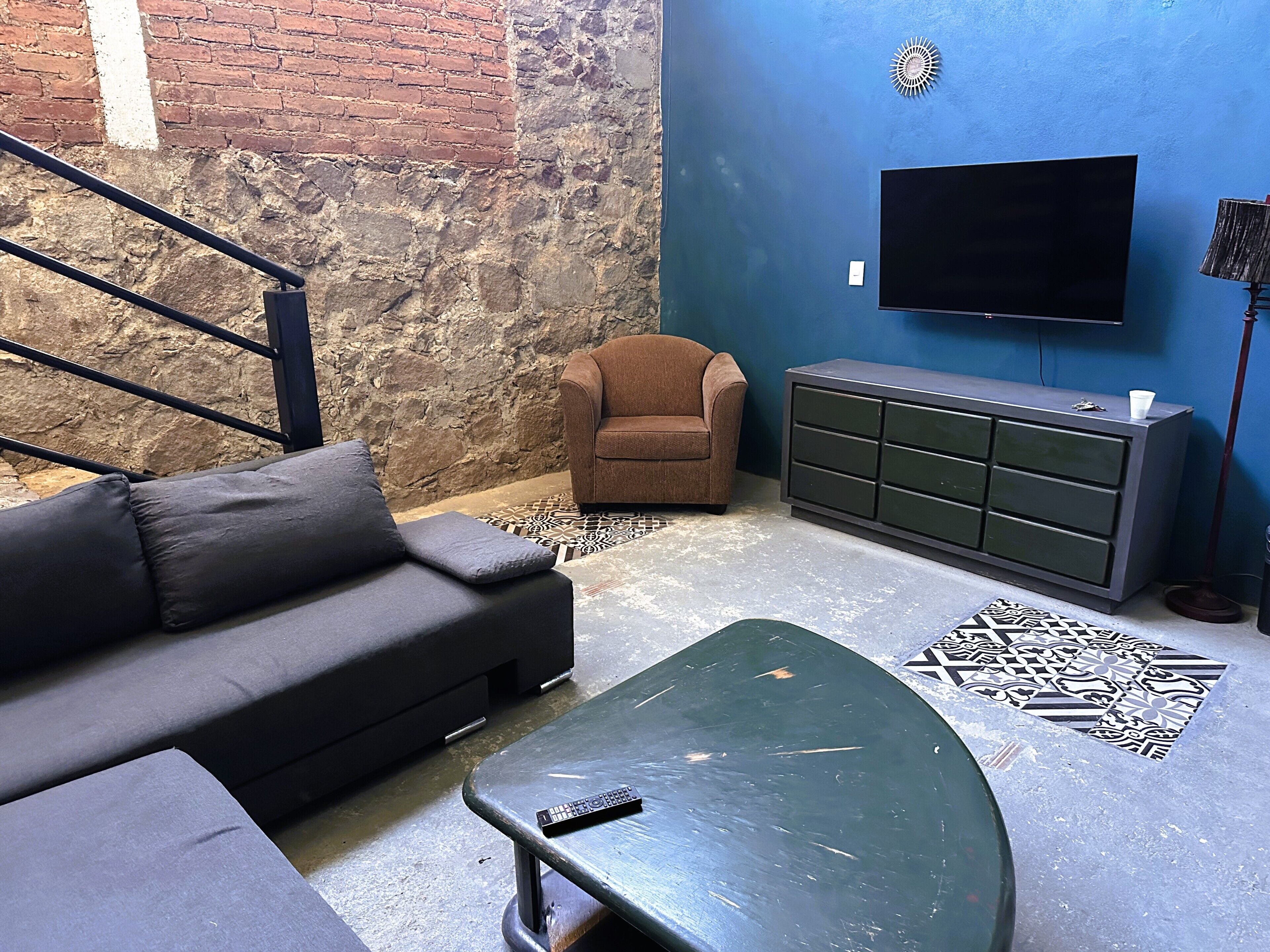 A living room with a sofa, a brown armchair, a green coffee table, a TV, and a cabinet.