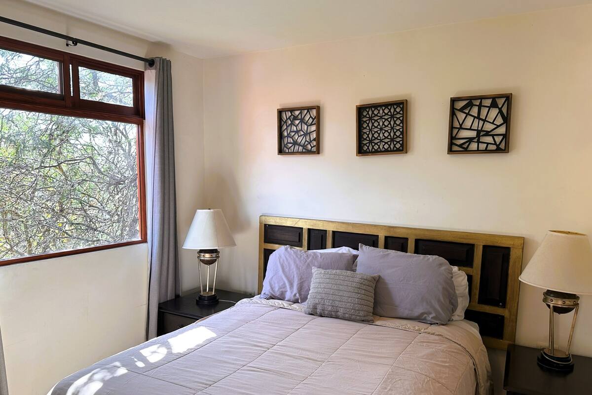Un dormitorio con una cama grande, dos mesitas de noche, un ventanal con cortinas y tres paneles decorativos en la pared.