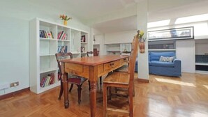A spacious living area with a wooden dining table, a blue sofa, and a bookshelf filled with books. - Anno Domini Appia Antica 120 sqm, large,  elegant, close to the historic center (Roma)
