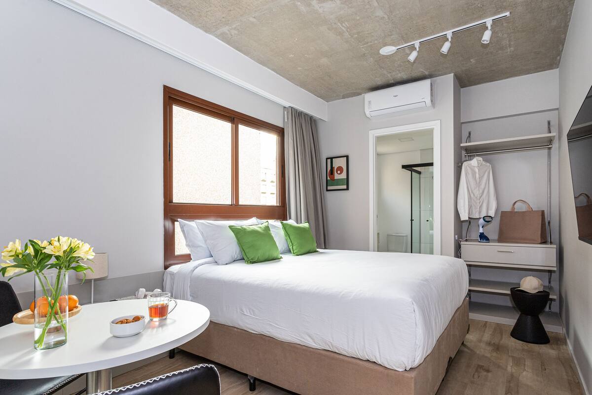 Ein modernes Hotelzimmer mit einem Bett, einem runden Tisch mit Blumenvase, einer kleinen Obstschale und einer Tasse Tee.