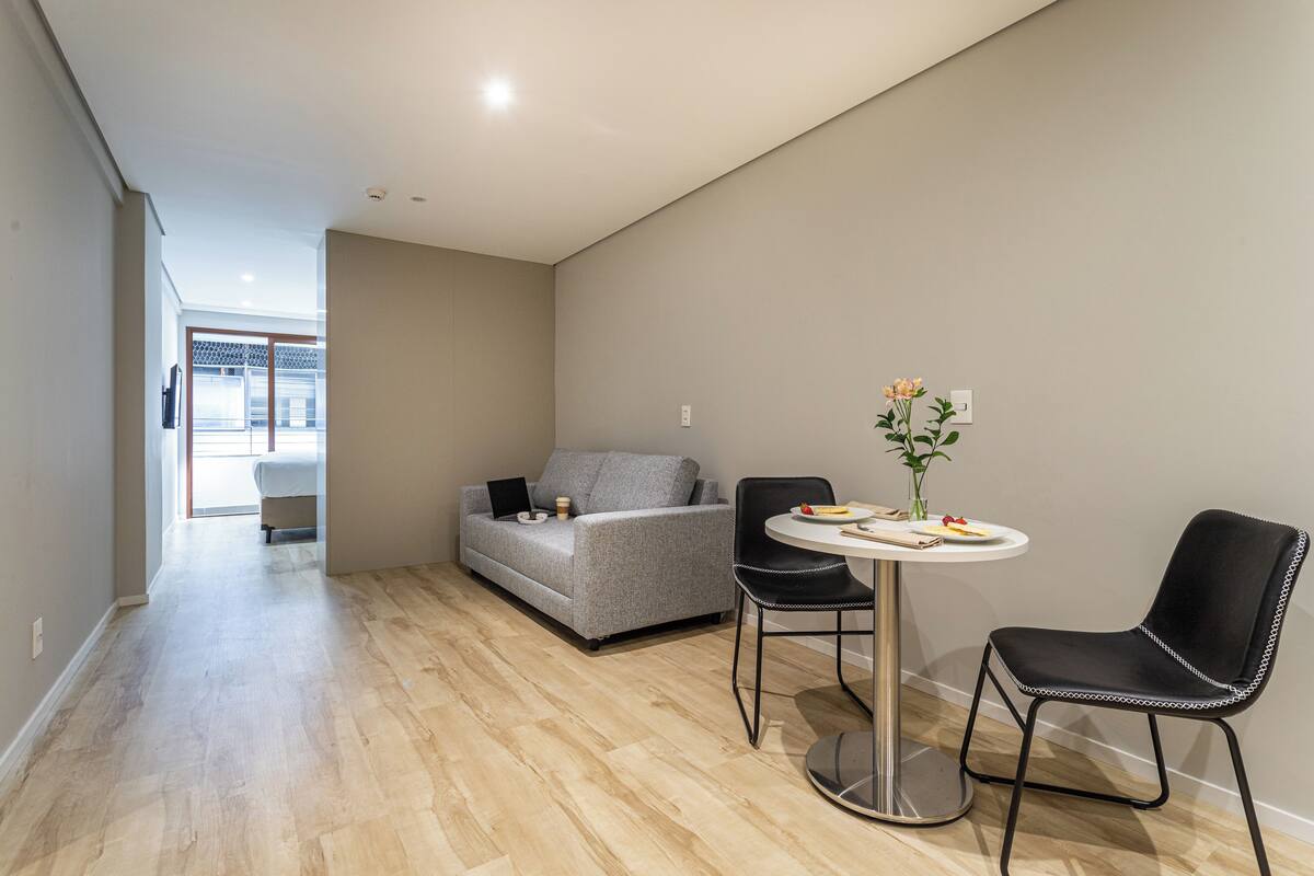 Ein modernes Wohnzimmer mit einem grauen Sofa, einem runden Tisch und zwei schwarzen Stühlen.