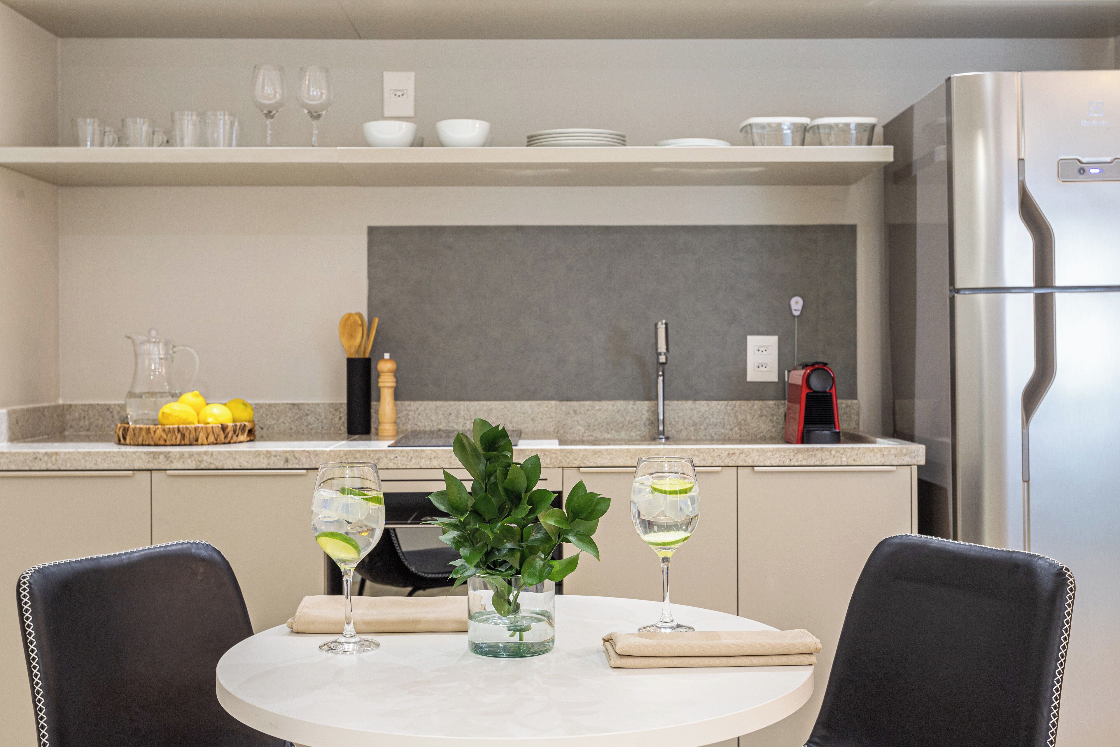 A modern kitchen with a round dining table, two chairs, a plant, and a refrigerator.