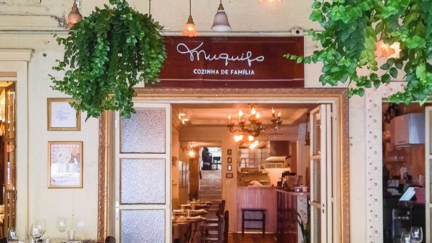 A restaurant interior with a tiled floor, hanging plants, and a sign reading "Miquelo Cozinha de Família." - Next Bela Cintra by Viva - Prédio completo com wi-fi próximo ao metrô Consolação e ao MASP (São Paulo)