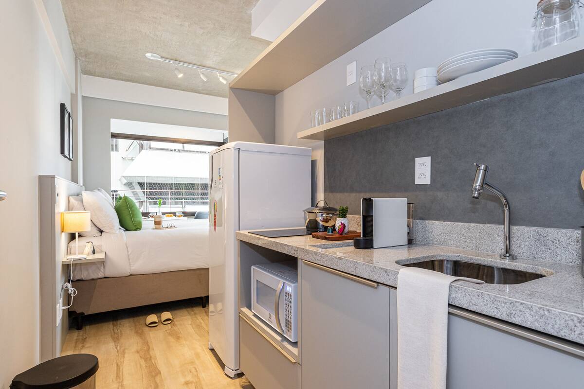 Eine kompakte Küche mit Kühlschrank, Mikrowelle, Spüle und einer Arbeitsplatte mit diversen Gegenständen.
