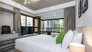A modern hotel room with a large bed, a desk with a flat-screen TV, a window with blinds, and a view of a building outside. - Next Bela Cintra by Viva - Prédio completo com wi-fi próximo ao metrô Consolação e ao MASP (São Paulo)