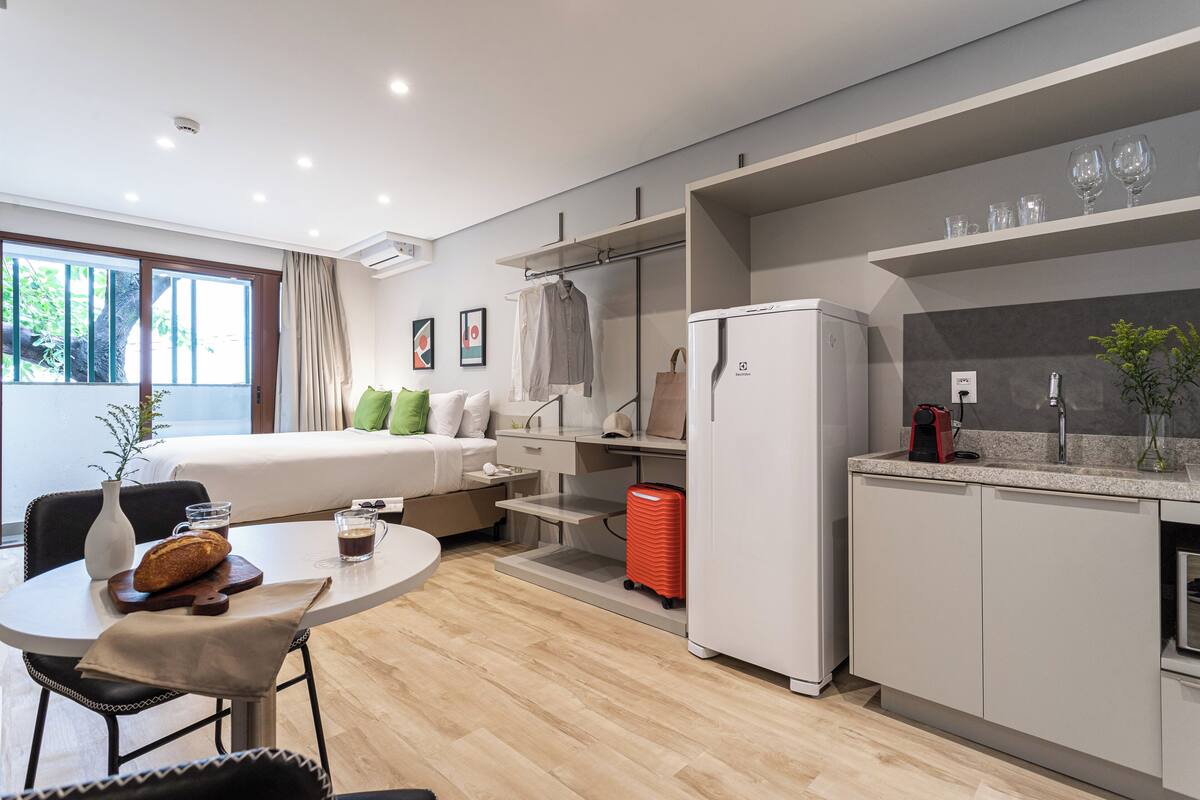 Ein modernes Hotelzimmer mit Bett, Frühstücksecke, Küchenzeile und Blick ins Grüne.
