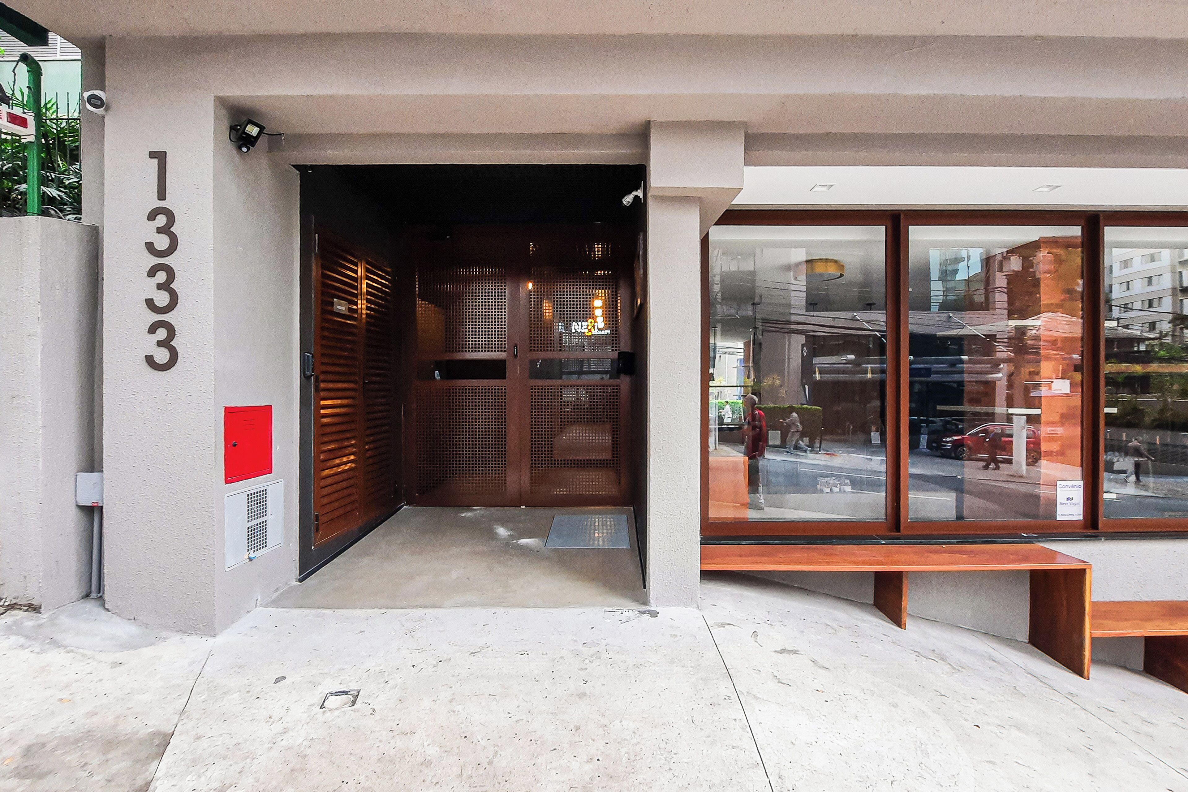 A building entrance with a number '1333' on the wall, a wooden door, and a bench outside.