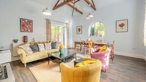 A spacious living room with a high ceiling, wooden beams, a sofa, a dining table with chairs, and a yellow armchair. - Blofield Cottage - UK48095 (Norwich)