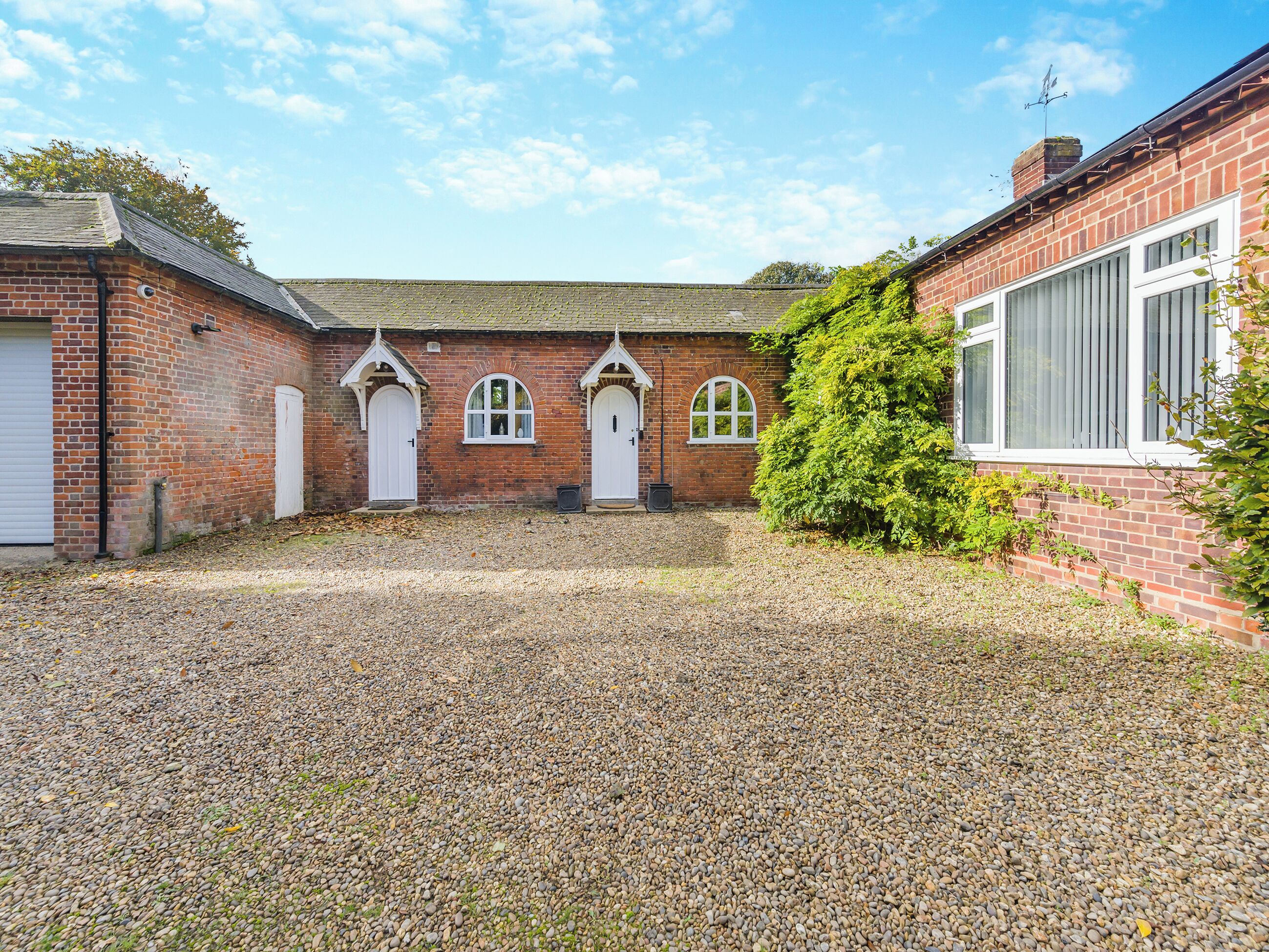 A courtyard with a gravel ground, a brick building with three arched doorways, and a large bush.