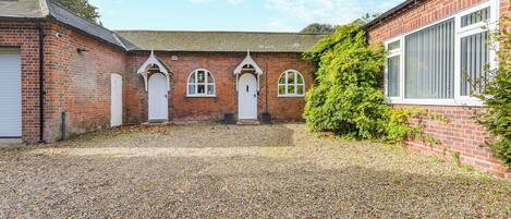 A courtyard with a gravel ground, a brick building with three arched doorways, and a large bush.