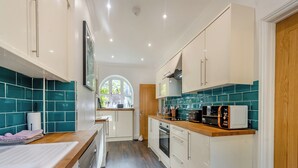 A modern kitchen with white cabinets, a wooden countertop, and teal backsplash tiles. - Blofield Cottage - UK48095 (Norwich)