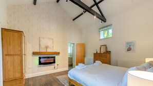 A bedroom with a bed, wooden wardrobe, a fireplace, a dresser, and a window. - Blofield Cottage - UK48095 (Norwich)