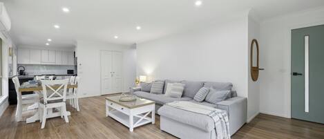 A modern living room with a grey sofa, white chairs, and a coffee table.