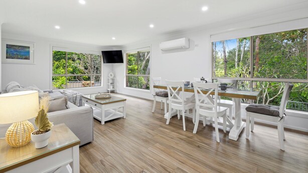A modern living room with a dining area, large windows, and a flat-screen TV.