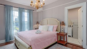 A bedroom with a bed, a chandelier, a nightstand, and a window with curtains.