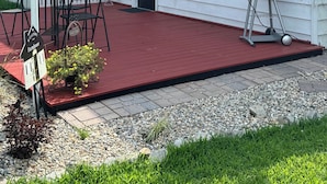 Une maison blanche avec un toit rouge, un patio couvert avec des meubles d’extérieur et un barbecue.