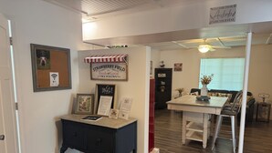 Une pièce chaleureuse avec un plancher en bois, une table noire sur laquelle est posé un menu encadré, un auvent rouge et blanc à rayures, et une enseigne accueillant les clients de l’Airbnb.