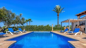Ein rechteckiger Swimmingpool mit blauen Kacheln, umgeben von weißen Liegestühlen und Palmen.