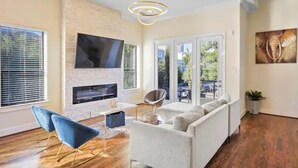 A modern living room with a fireplace, a sofa, a TV, and a dining area with a view of the outdoors. - Luxury Midtown Gem : Amazing Rooftop Views (Houston)