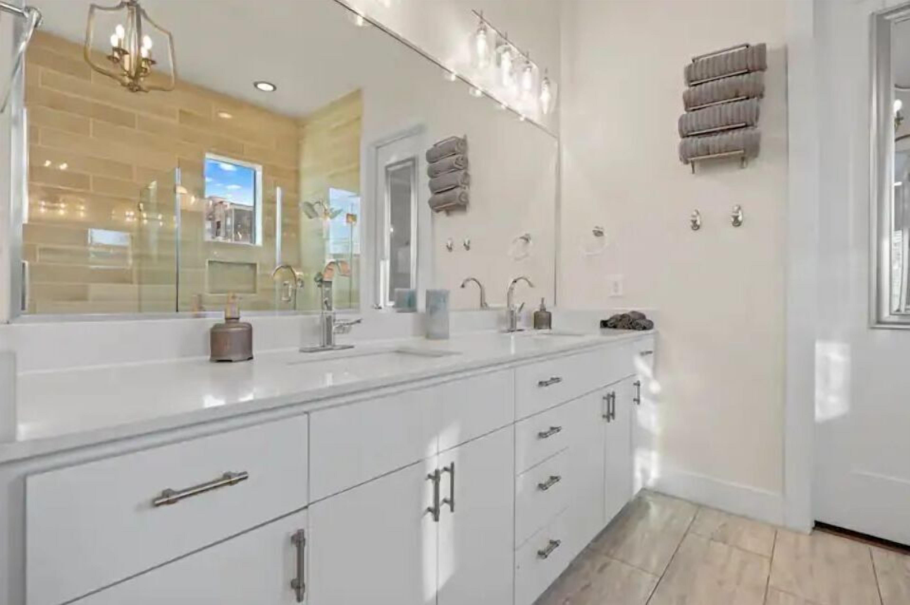 Une salle de bain moderne avec un grand miroir, des meubles blancs et un espace douche.