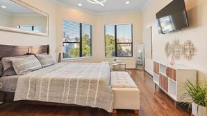A modern bedroom with a large bed, a TV mounted on the wall, and a window with blinds. - Luxury Midtown Gem : Amazing Rooftop Views (Houston)