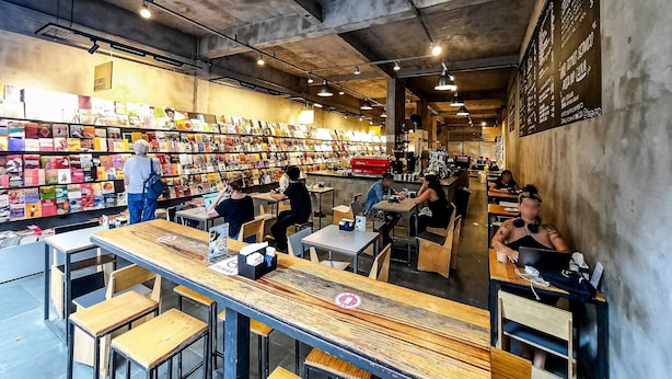 A bookstore café with tables and chairs, bookshelves, and a menu on the wall. - Zoom Santa Cecília by Viva - Prédio próximo à estação Marechal Deodoro e Fácil acesso ao Memorial da América Latina (São Paulo)