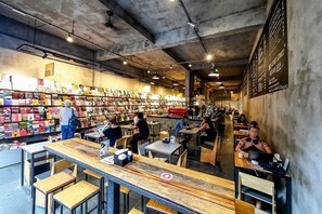 Una cafetería con librería, con mesas y sillas, estanterías llenas de libros y un menú en la pared.