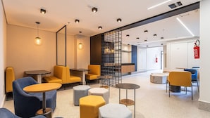 A modern lounge area with seating arrangements, tables, and a fire extinguisher mounted on the wall. - Zoom Santa Cecília by Viva - Prédio próximo à estação Marechal Deodoro e Fácil acesso ao Memorial da América Latina (São Paulo)