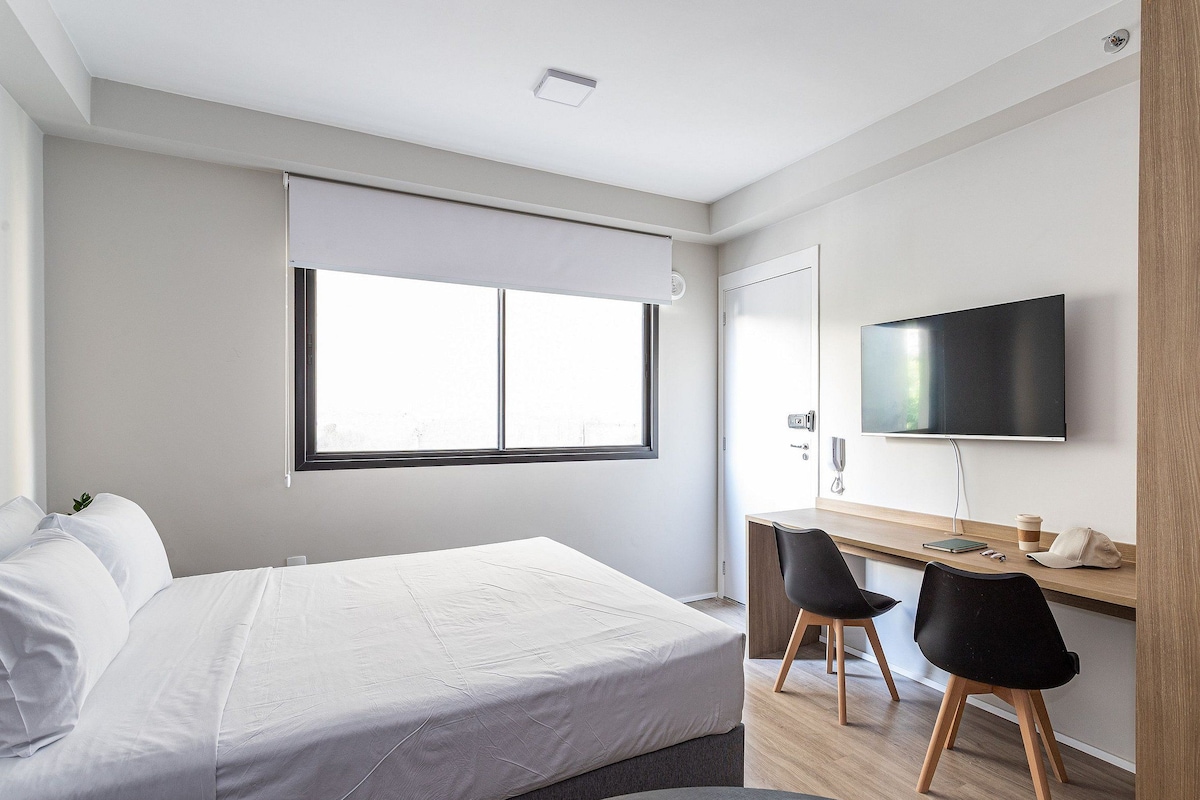 A modern bedroom with a bed, a desk, and a TV.