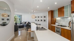 A modern kitchen with a central island, stainless steel appliances, and wooden cabinets. - 2 Bedroom Garden & Pool View (Casuarina)
