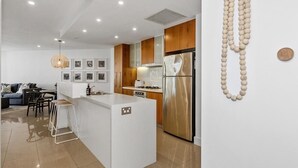 A modern kitchen with a central island, wooden cabinets, stainless steel appliances, and a pendant light. - 2 Bedroom Garden & Pool View (Casuarina)