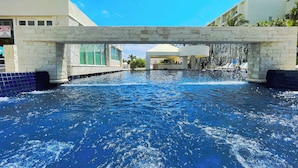 A swimming pool with a stone bridge overhead, surrounded by buildings.