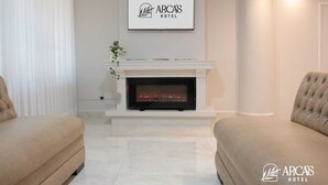 A modern living room with a fireplace, two beige sofas, and a framed logo of Arca's Hotel on the wall.