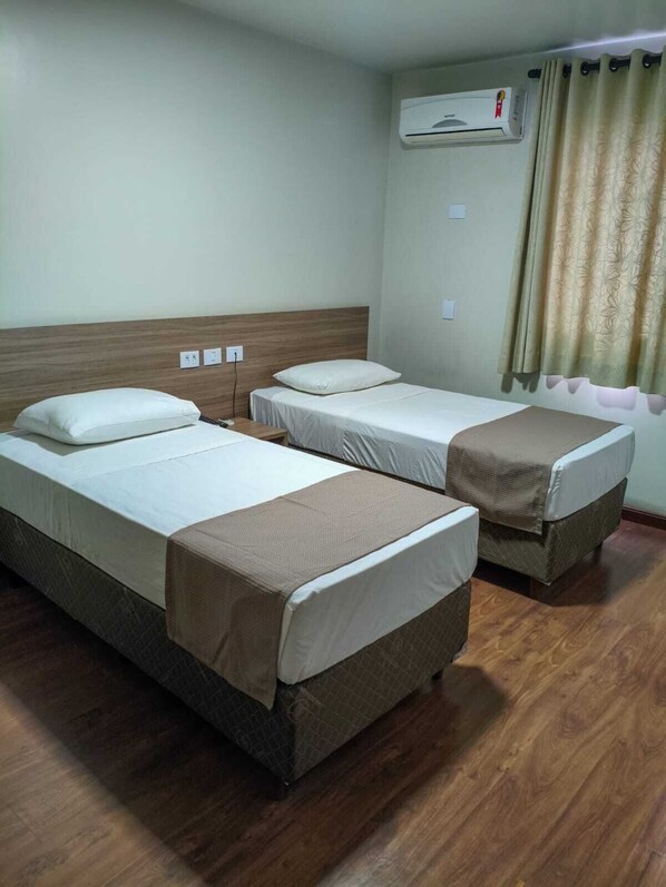 Una habitación de hotel con dos camas individuales, un cabecero de madera, un equipo de aire acondicionado y una cortina.