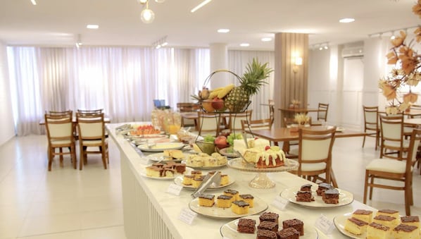 A buffet setup in a hotel with various desserts and fruits displayed on a long counter.