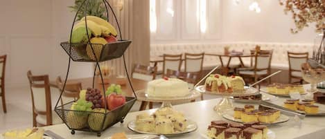 Una mesa de bufé con diversos postres y frutas, entre ellos pasteles, tartas y una cesta de frutas.