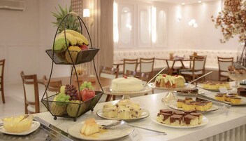 Una mesa de bufé con diversos postres y frutas, entre ellos pasteles, tartas y una cesta de frutas.