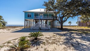 A two-story house with a balcony, a staircase leading to the entrance, and a sandy beach in the background. - Sunset View Beach House in Ocean Springs - Beachfront property (Ocean Springs)