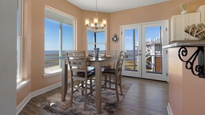 A dining area with a table and chairs, a chandelier, and a view of the beach through large windows. - Sunset View Beach House in Ocean Springs - Beachfront property (Ocean Springs)