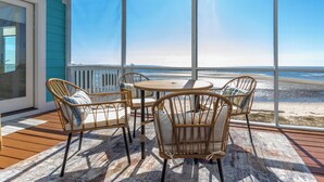 A sunlit room with a large window overlooking a beach, furnished with wicker chairs and a round table. - Sunset View Beach House in Ocean Springs - Beachfront property (Ocean Springs)