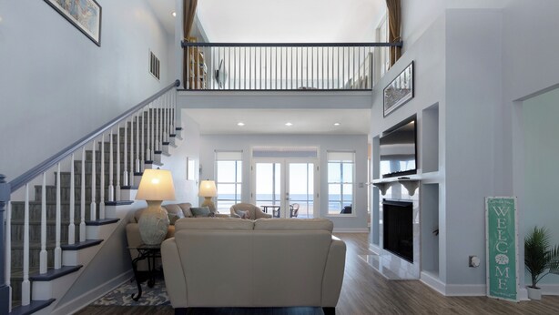 A spacious living area with a staircase, a sofa, a fireplace, and a view of the outdoors. - Sunset View Beach House in Ocean Springs - Beachfront property (Ocean Springs)