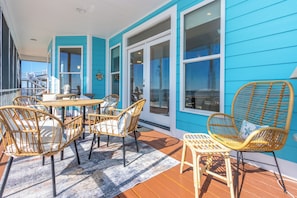 A covered outdoor area with a wooden table and wicker chairs, a blue exterior wall, and large windows. - Sunset View Beach House in Ocean Springs - Beachfront property (Ocean Springs)