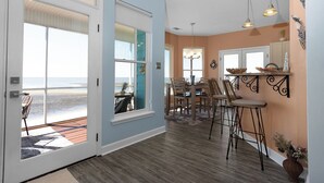 A coastal home interior with a dining area, kitchen, and large sliding glass doors leading to a beach view. - Sunset View Beach House in Ocean Springs - Beachfront property (Ocean Springs)