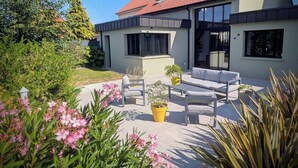 A modern house with a red-tiled roof, a patio with outdoor furniture, and a garden with pink flowers. - Industrial-style B&B in Peuplingues (Peuplingues)