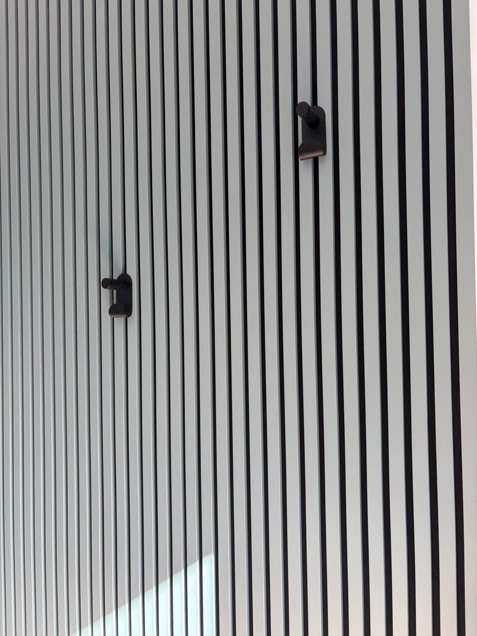 Eine Wand mit vertikalen schwarz-weißen Streifen und zwei schwarzen, an der Wand befestigten Objekten.