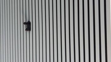 Eine Wand mit vertikalen schwarz-weißen Streifen und zwei schwarzen, an der Wand befestigten Objekten.